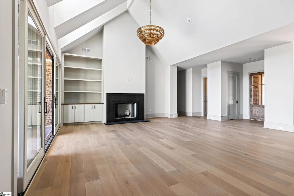 Great room with vaulted ceiling, white oak floors and black fireplace flanked by built-in shelving