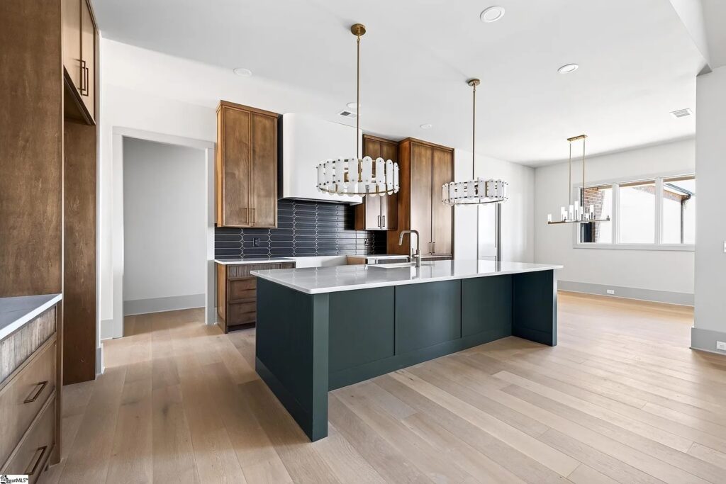 Kitchen with deep green island, warm wood cabinetry, white countertops and statement chandeliers